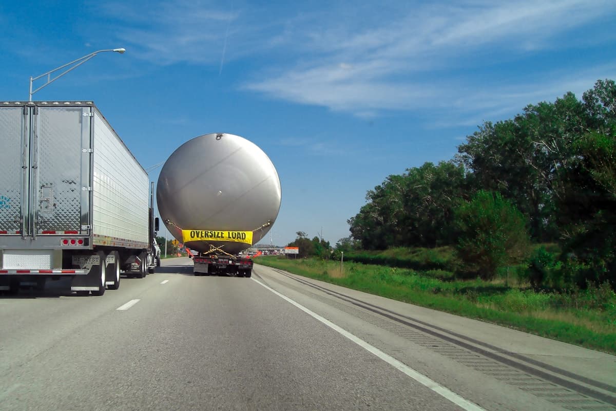 A lowbed trailer transporting an oversized industrial load along a UAE highway with escort vehicle nearby